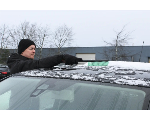 Man tar bort snö från ett biltak med en snöborste