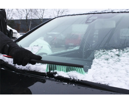 En person tar bort snö från en vindruta med en snöborste.