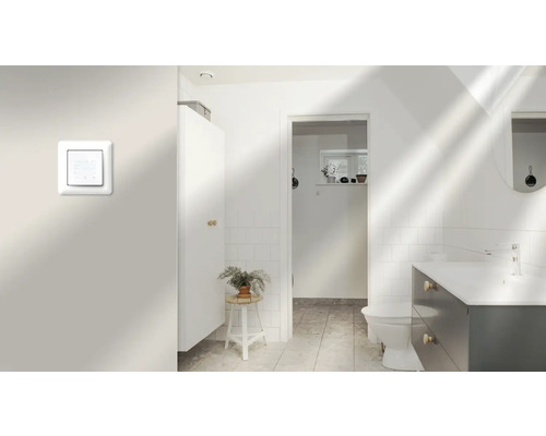 Ljust badrum med handfat, toalett och elektronisk rumstermostat på väggen