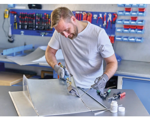 Hantverkare som löder metalldelar i en verkstad med verktyg och arbetsbänk