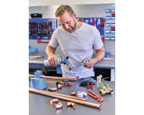 Man som löder kopparrör med en gasbrännare, omgiven av kopparrörskopplingar och verktyg