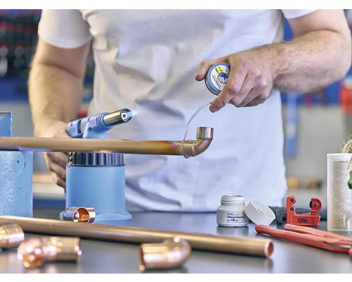 Hantverkare löder kopparrör med lödlampa och lödtenn