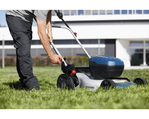 En person använder en batteridriven gräsklippare på en gräsmatta framför ett hus.