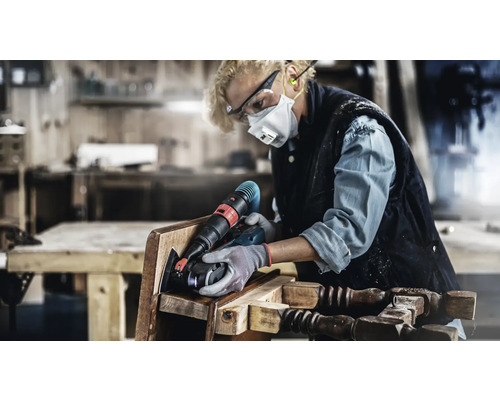 Kvinna slipar en stol med ett elverktyg i en verkstad