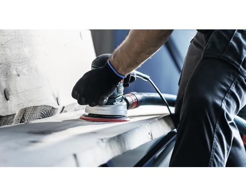 En person slipar ett arbetsstycke med en excenterslipmaskin.