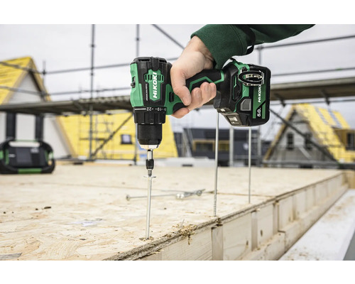 En hantverkare använder en HiKoki sladdlös skruvdragare på en byggarbetsplats för att skruva en lång skruv i trä.