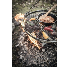 Hängande grill över öppen eld med biff, grönsaker och bönor i en panna.