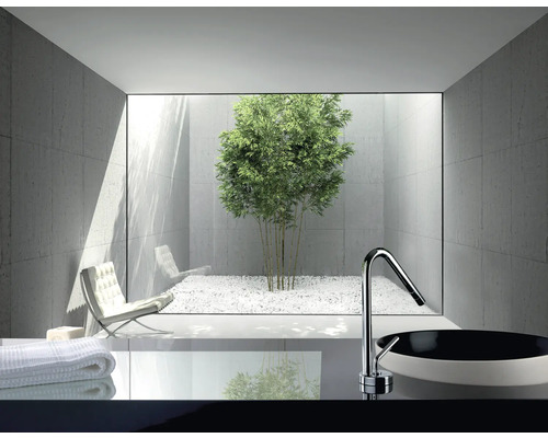 Modernt badrum med handfat, armatur och utsikt över en innergård med bambu och vitt grus