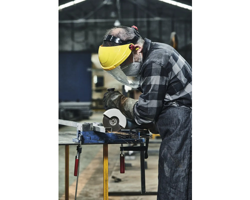 Hantverkare med skyddsvisir och handskar skär metall med en slipmaskin på ett skruvstäd.