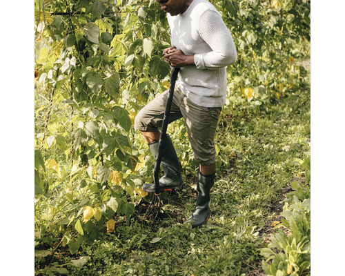 En man i gummistövlar använder en grepe i trädgården.