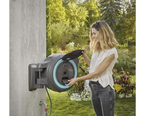 Kvinna som använder en väggmonterad slangvinda från Gardena i trädgården.