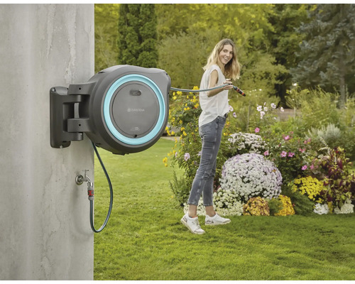 Gardena slangbox på väggen med kvinna som vattnar trädgården