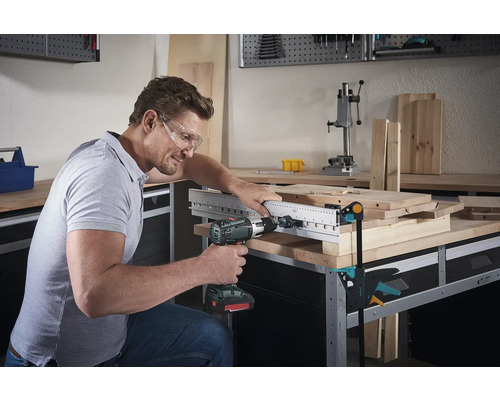 Man borrar med en borrmaskin genom en träskiva med borrfixtur på en arbetsbänk.