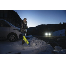 Kvinna skottar snö med en snöskyffel bredvid en bil.