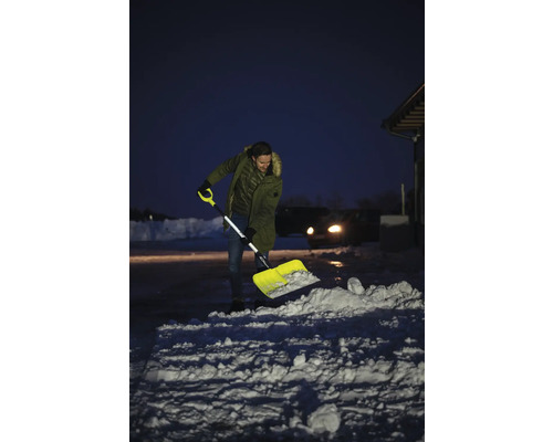 Man skottar snö med en snöskyffel framför ett hus