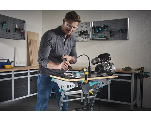 En man arbetar med ett multifunktionellt verktyg på ett arbetsstycke på en Wolfcraft arbetsbänk i en verkstad.