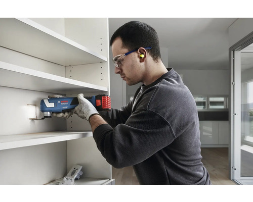En man använder ett multifunktionsverktyg för att såga i en hylla.