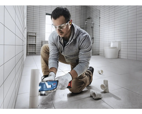 En man använder ett multifunktionellt verktyg i badrummet för att skära av ett rör.