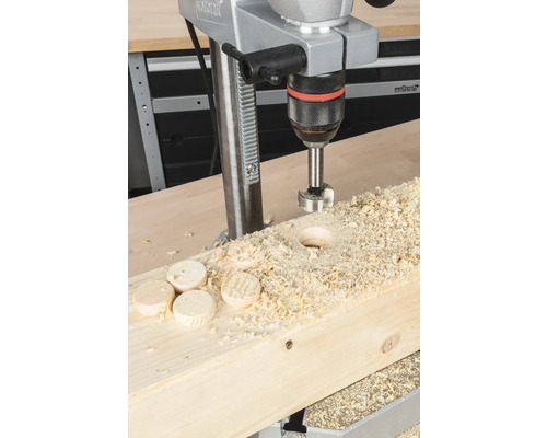 Bordsborrmaskin som borrar ett hål i en träbräda med träflisor och träskivor