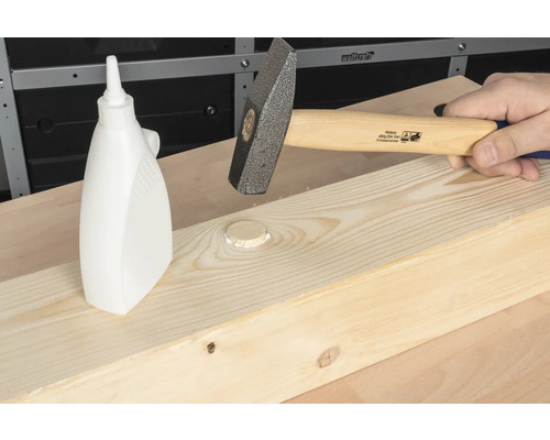 En hammare slår en träplugg med trälim i en träplanka.