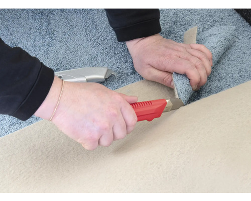 Två händer skär en matta med en mattkniv.