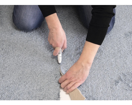 En person skär en matta med en mattkniv.