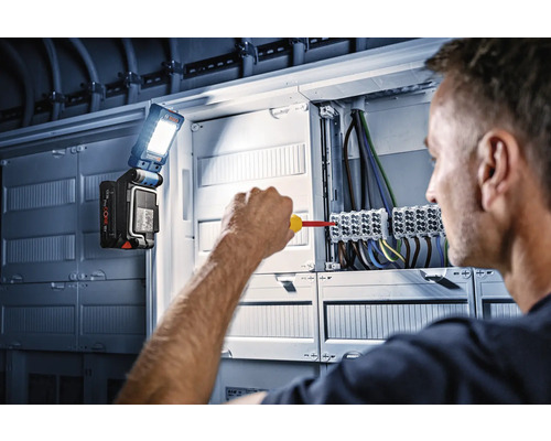 En elektriker arbetar på en kopplingsdosa med en Bosch arbetslampa.