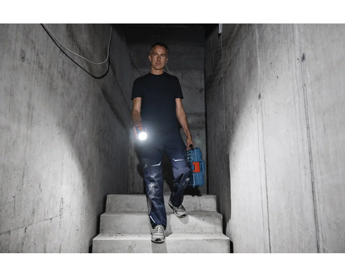 Man går nerför en betongtrappa med ficklampa och verktygslåda