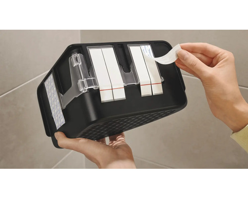 Person tar bort skyddsfilmen från tejp på en svart hylla för badrumstillbehör.