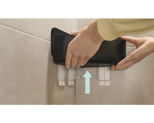 En person fäster en svart badrumshylla på väggen.