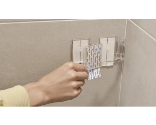 Person fäster självhäftande remsor på ett fäste i badrummet.