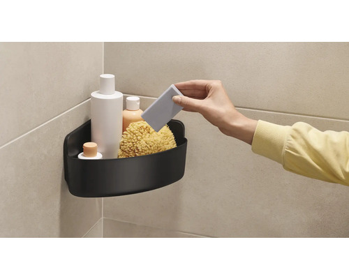 Hörn med svart duschhylla, fylld med badprodukter och en badsvamp