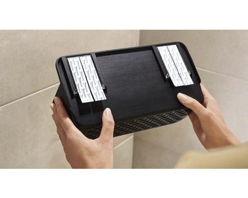 Person som fäster svart väggfläkt med självhäftande remsor på väggen