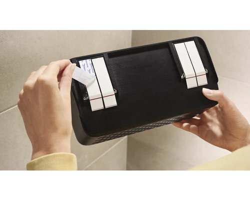 Person fäster en svart vägghylla med självhäftande remsor på en vägg