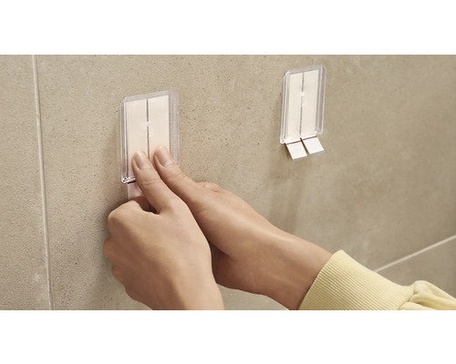 En person fäster en självhäftande krok på en vägg