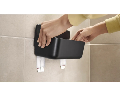 Person monterar en svart förvaringslåda på väggen med självhäftande fäste