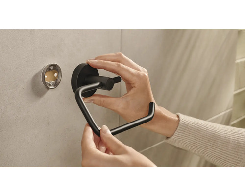 En person monterar en svart toalettpappershållare på en vägg.