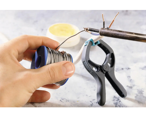 Lödtennrulle i handen, lödarbete på en kabel fixerad med en klämma