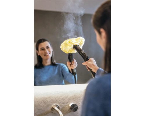 Kvinna använder en ångtvätt med gult tygfäste på en spegel i badrummet