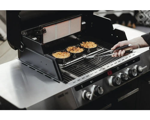 En grill med tre små gratängformar på grillgallret som flyttas med en tång.