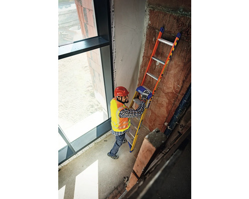 En man med hjälm och säkerhetsväst står på en stege i en byggnad.