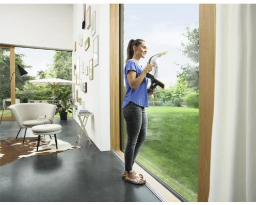 Kvinna rengör fönster med en fönstertvätt i ett ljust vardagsrum.