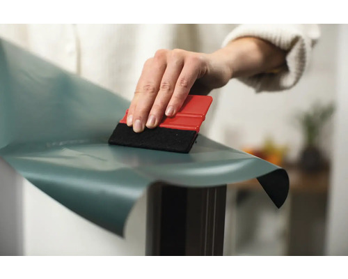 Person jämnar ut självhäftande film med en skrapa