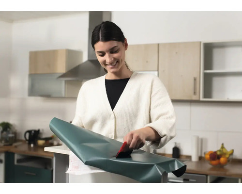 Kvinna applicerar dekorativ film med en skrapa i köket