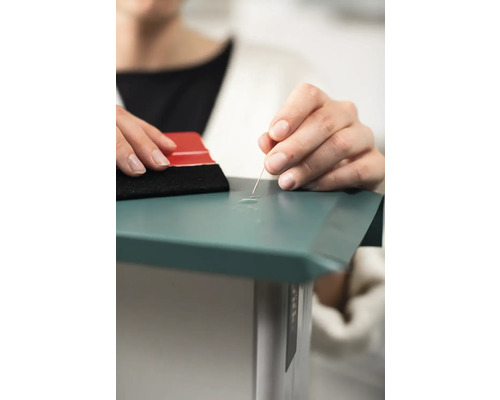 En person använder en nål och en skrapa för att ta bort luftbubblor under en film.