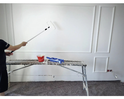 Målare målar en vägg med en färgroller, hink och färgtråg är redo