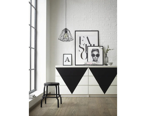 Interiörbild av ett rum med en byrå med geometriska mönster, en pall, affischer och en pendellampa.