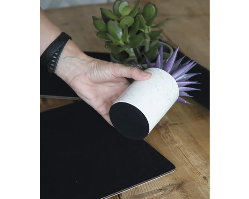 Dekorativt arrangemang med konstgjord växt i vit kruka och svart bordsduk.