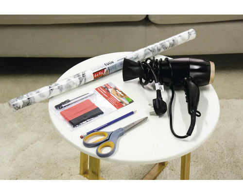 Dekorativ film, skrapa, skärare, sax, penna och hårtork på ett bord