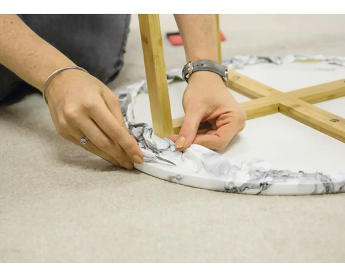 En person skär av förpackningen från ett runt bord med träben.